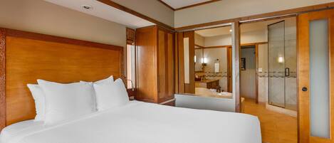 A hotel room with a large bed, a wooden headboard, a bathroom with a glass shower, and a mirror.