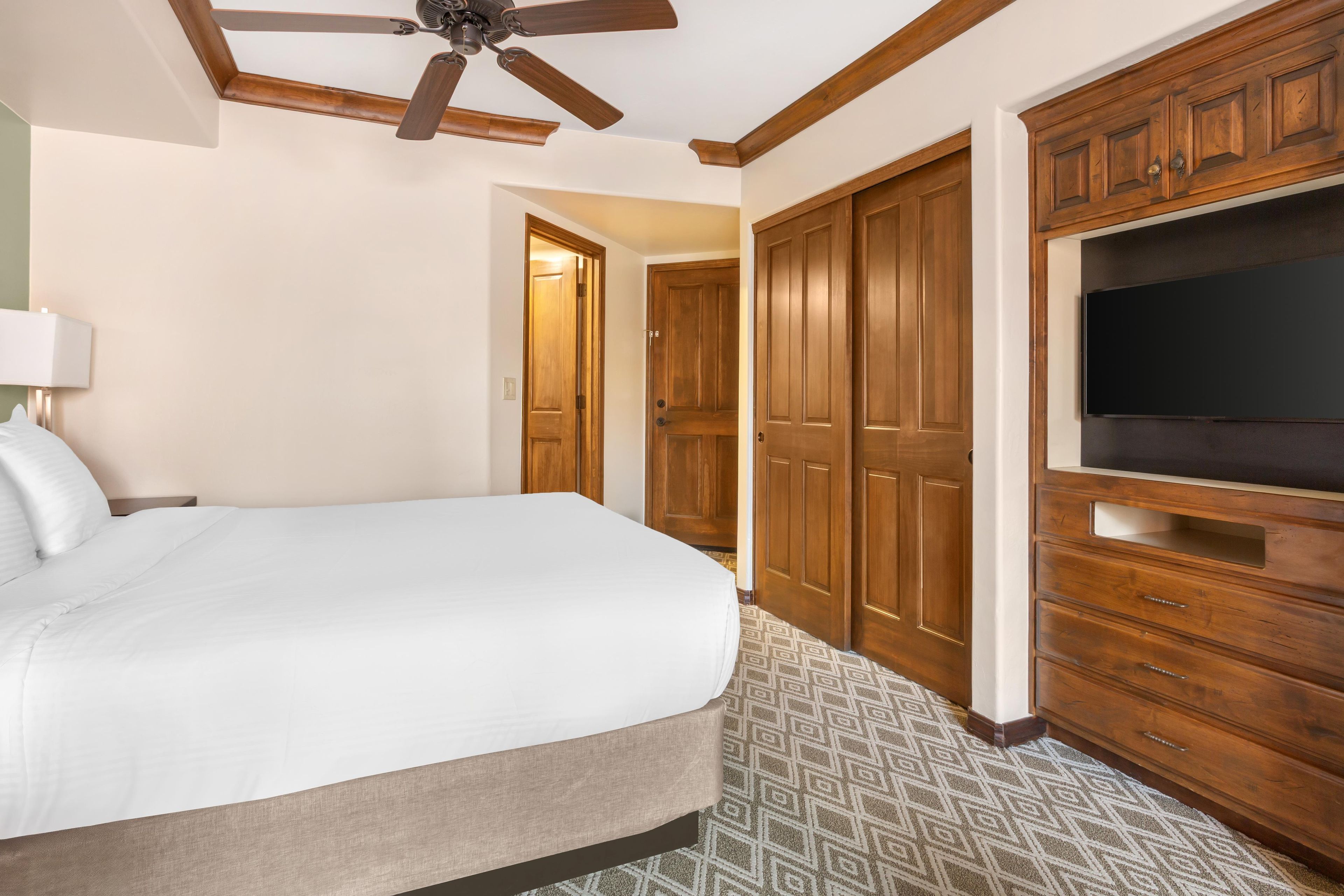Une chambre d’hôtel équipée d’un lit, d’une télévision, d’armoires en bois et d’un ventilateur de plafond.