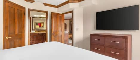 A bedroom with a large bed, wooden wardrobe, a flat-screen TV, and a ceiling fan.