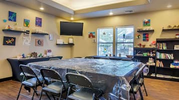A conference room with a large table, chairs, a bookshelf, and artwork on the walls.