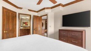 A bedroom with a large bed, wooden wardrobe, a flat-screen TV, and a ceiling fan.