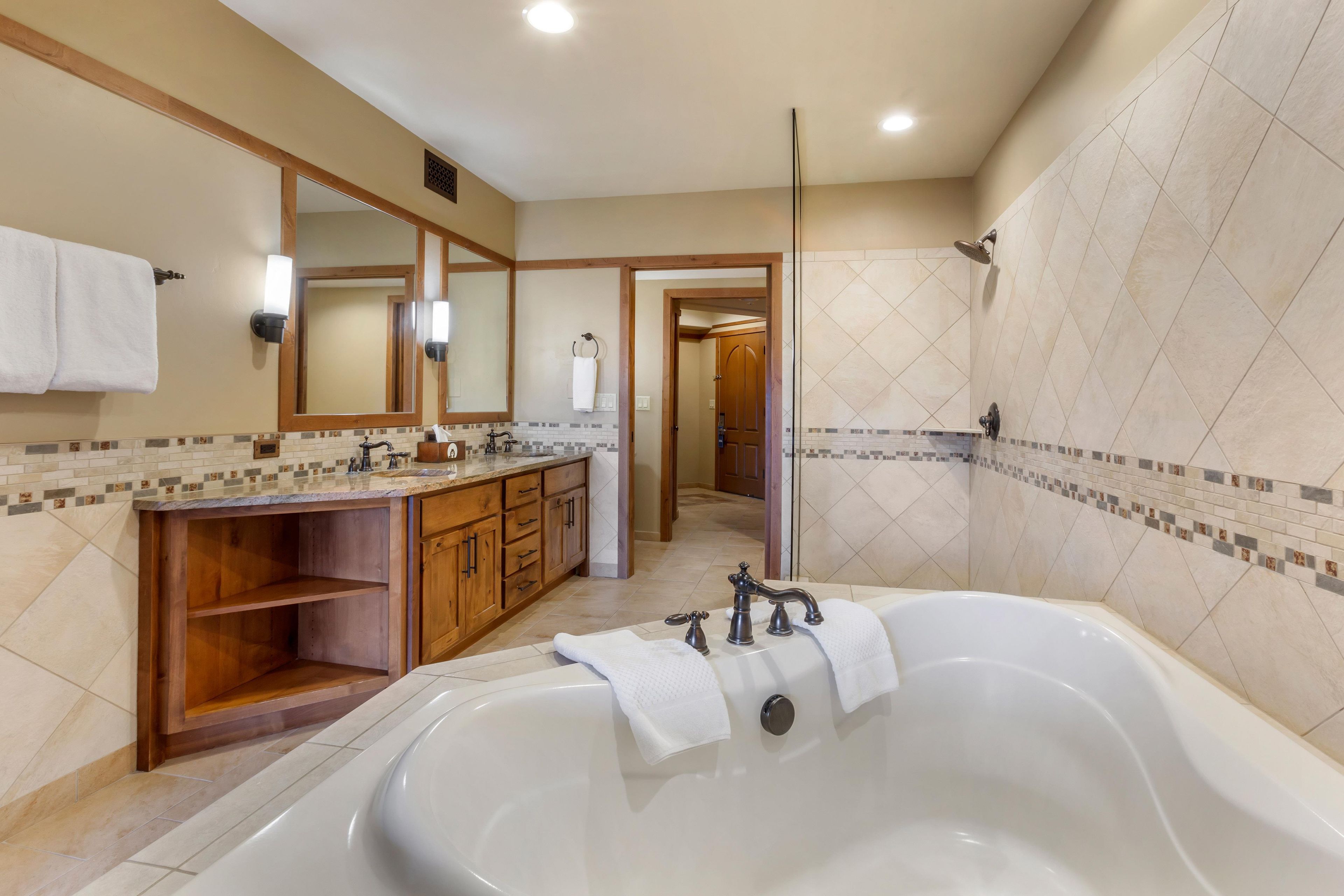 A modern bathroom with a large bathtub, wooden vanity, and a shower area.