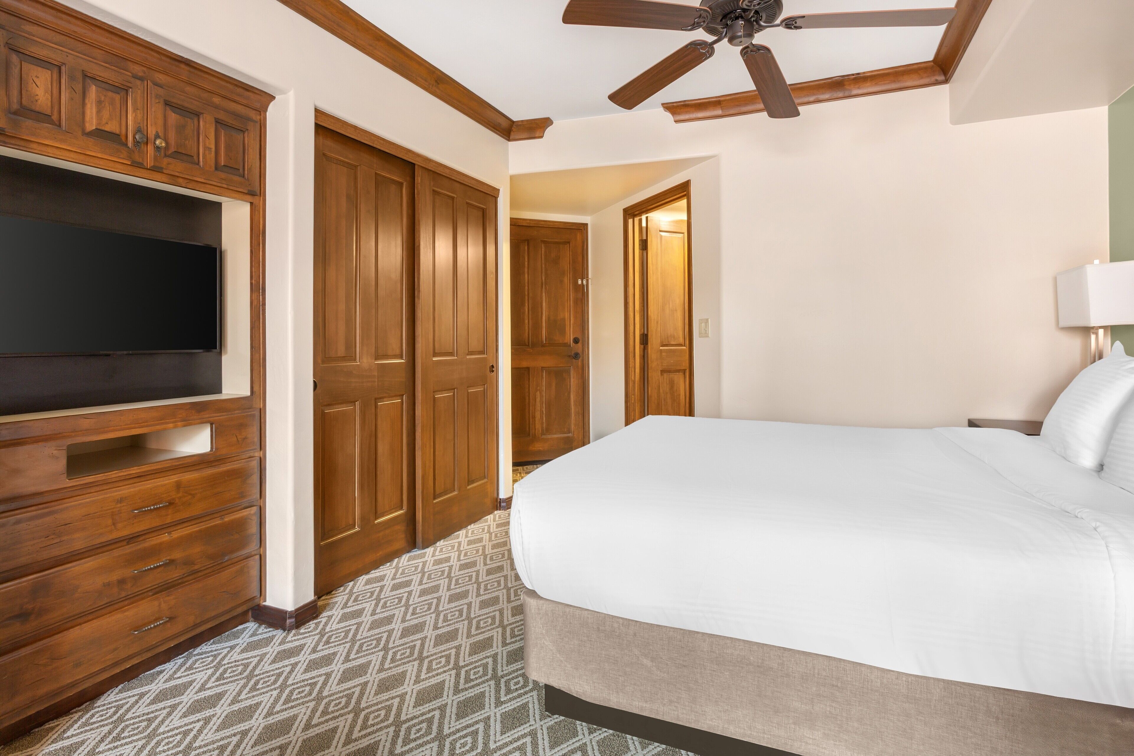 Habitación de hotel con una cama grande, armario de madera, ventilador de techo y televisor.