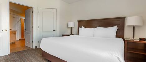 A hotel room with a large bed, two bedside tables with lamps, a wooden headboard, and a door leading to a hallway.