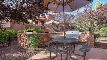 Patio esterno con tavolo rotondo e sedie, un barbecue e un grande ombrellone che offre ombra.