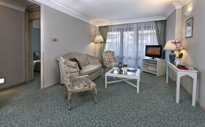 A hotel room with a sofa, armchair, coffee table, TV, and a small side table with decorative items. - Apart Hotel Best (Ankara)