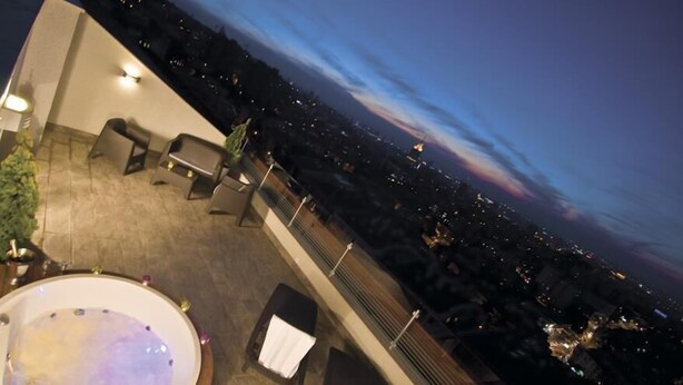 A rooftop terrace with a hot tub, seating area, and a city view at dusk.