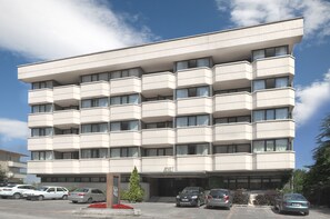A multi-story hotel with a flat facade, balconies, and a parking area with several cars. - Apart Hotel Best (Ankara)