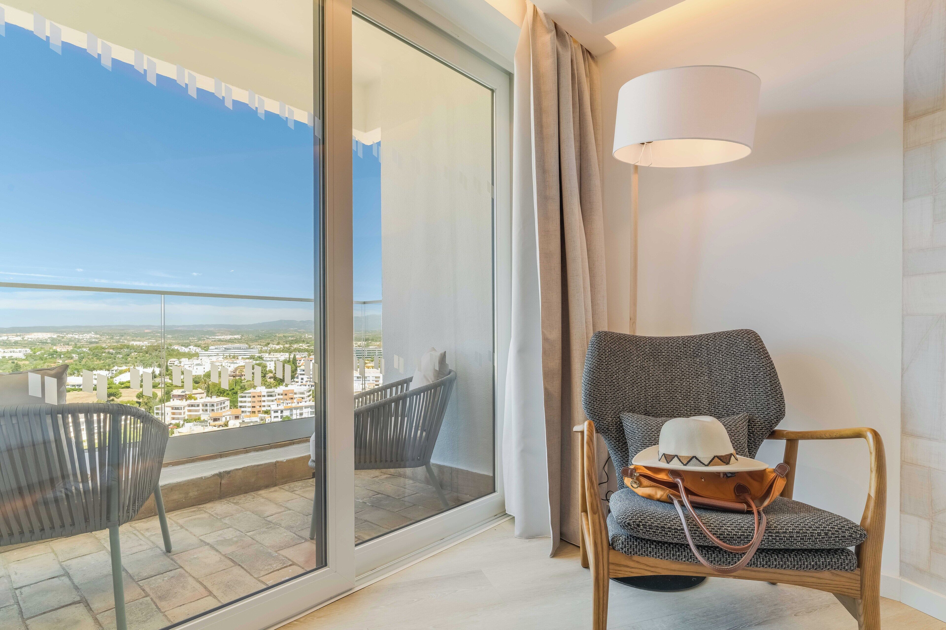 Een balkon met uitzicht op een stadsbeeld, een stoel met een handtas, en een moderne lamp.