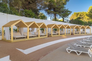 A row of wooden beach cabanas with white cushions and curtains, lined up along a sandy beach with lounge chairs in the foreground. - Pestana Blue Alvor Beach - All Inclusive Hotel (Portimão)
