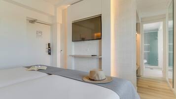 Una habitación de hotel moderna con una cama grande, un televisor de pantalla plana montado en la pared, un estante pequeño y una puerta que da a un baño.