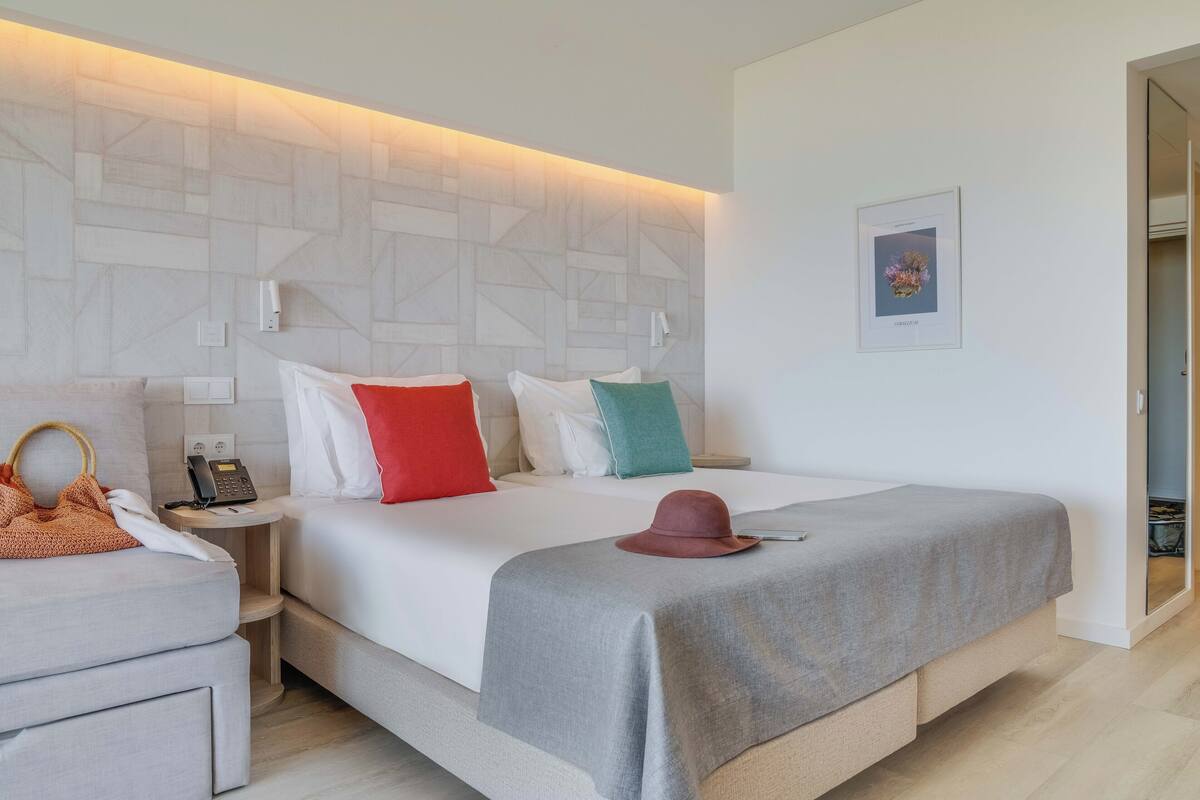 A hotel room with a bed, bedside tables, a telephone, a hat, and a framed picture on the wall.