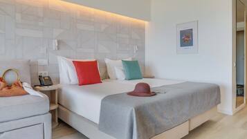 A modern hotel room with a large bed, a bedside table with a phone, a small table with a hat, and a framed picture on the wall.