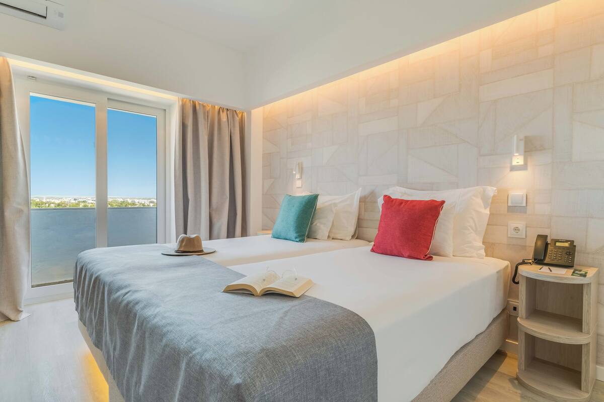 A hotel room with two beds, a large window, and a view of the city.