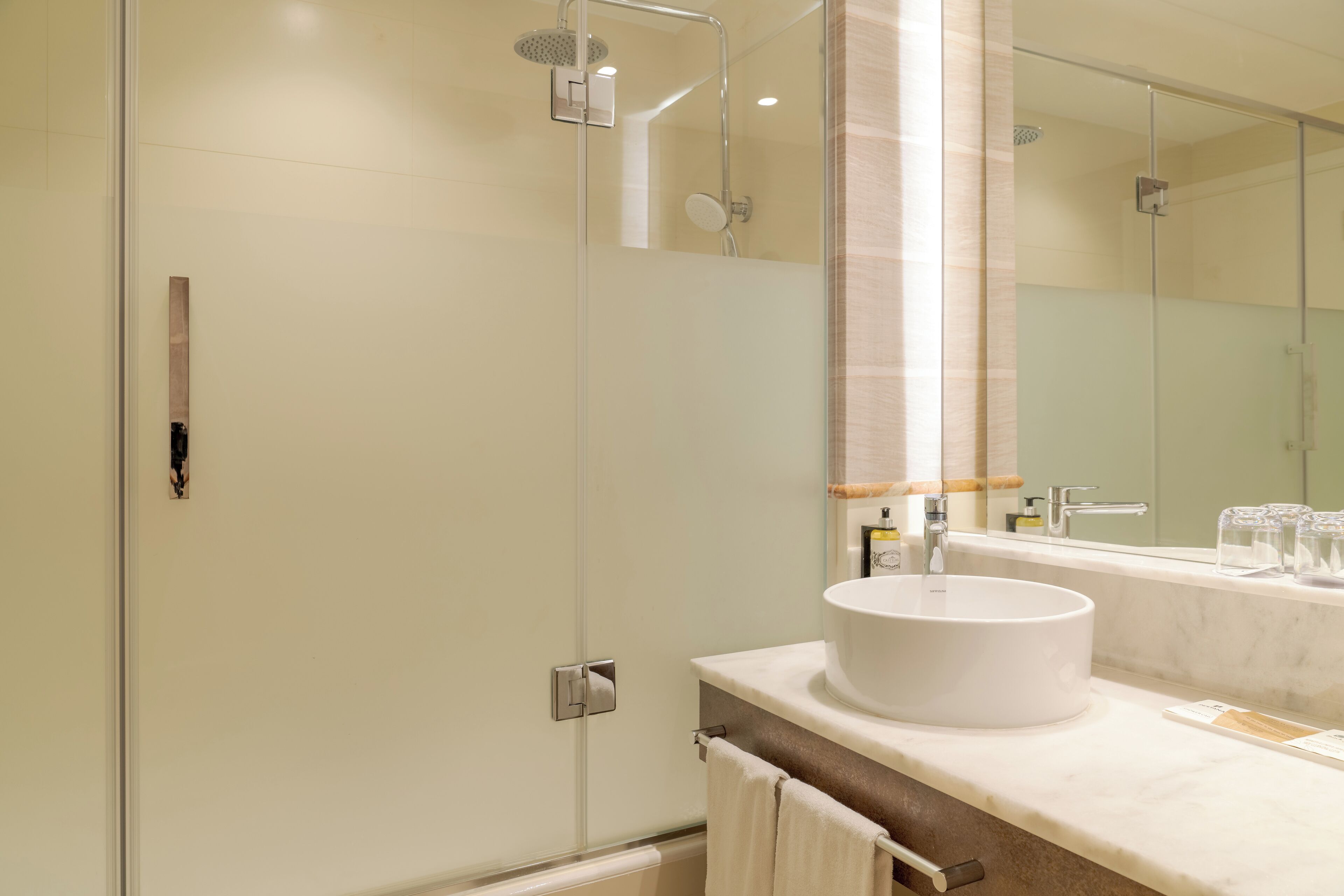 Un baño moderno con cabina de ducha de vidrio, un lavamanos blanco y un espejo grande.