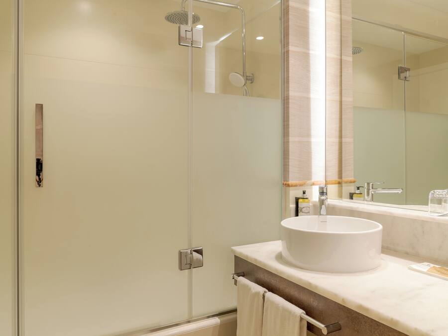 Un baño moderno con cabina de ducha de vidrio, un lavamanos blanco y un espejo grande.