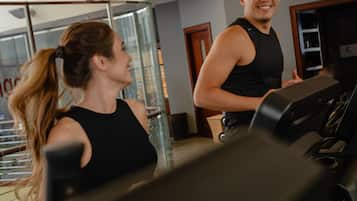 A gym with treadmills, a woman and a man exercising, and a wall with motivational text.