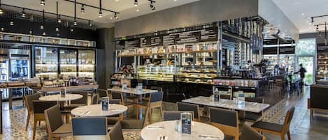 Un restaurante moderno con mesas y sillas redondas, una zona de bar y una exhibición de alimentos.