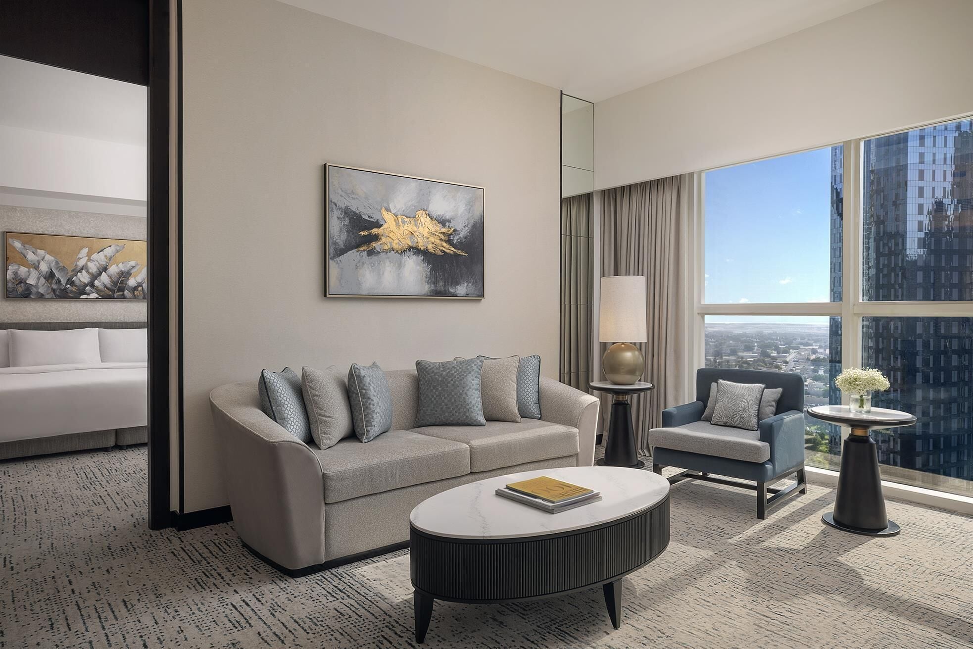 A modern hotel room with a sofa, armchair, and a round coffee table.