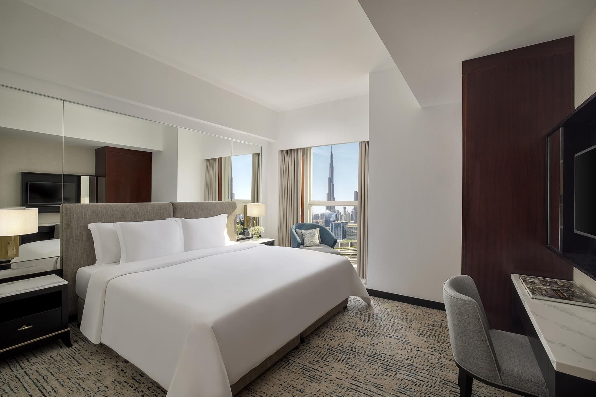 Quarto de hotel com uma cama grande, uma escrivaninha, uma cadeira, uma televisão e vista para a cidade.
