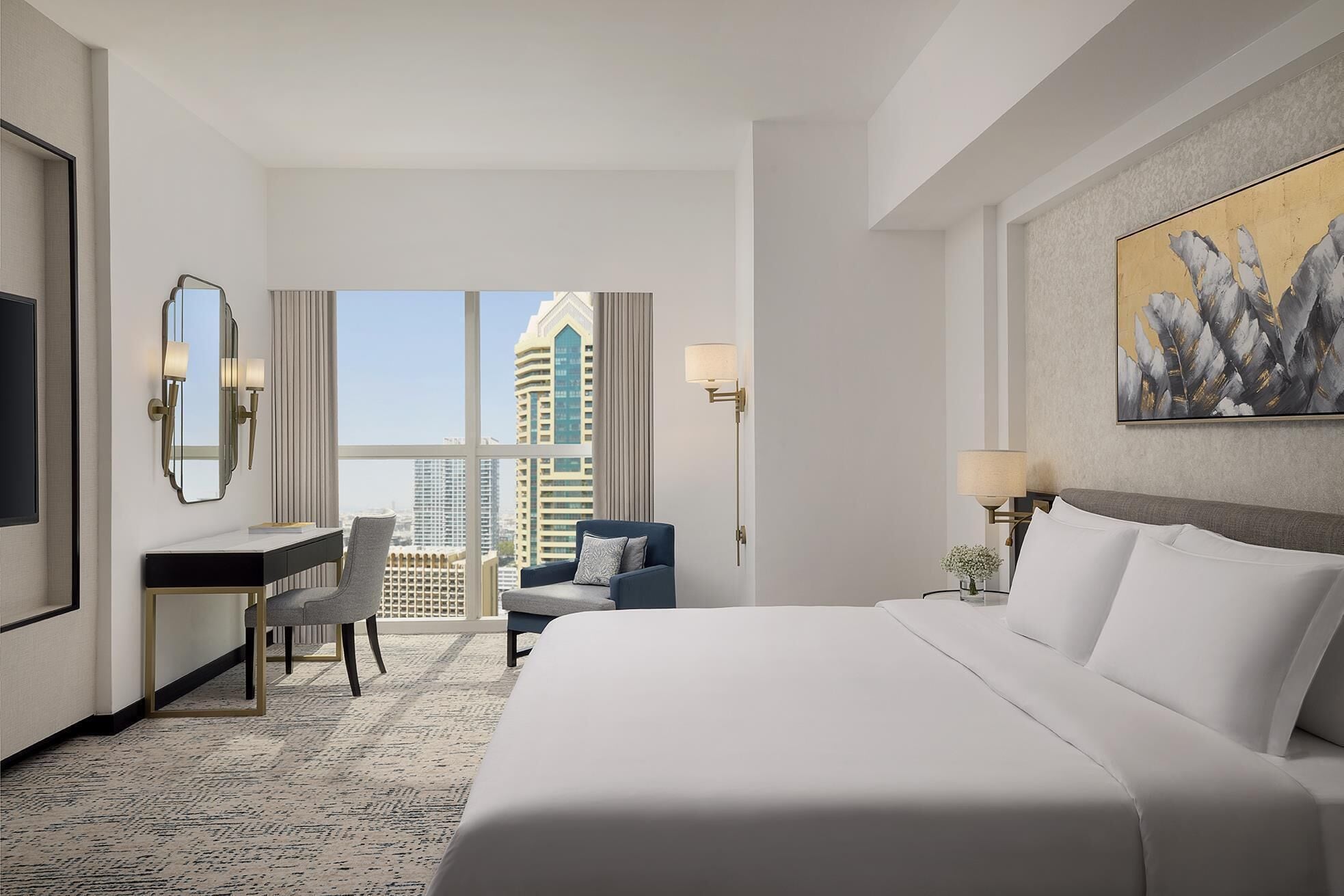 A hotel room with a bed, a desk, a chair, a nightstand, a lamp, and a painting.