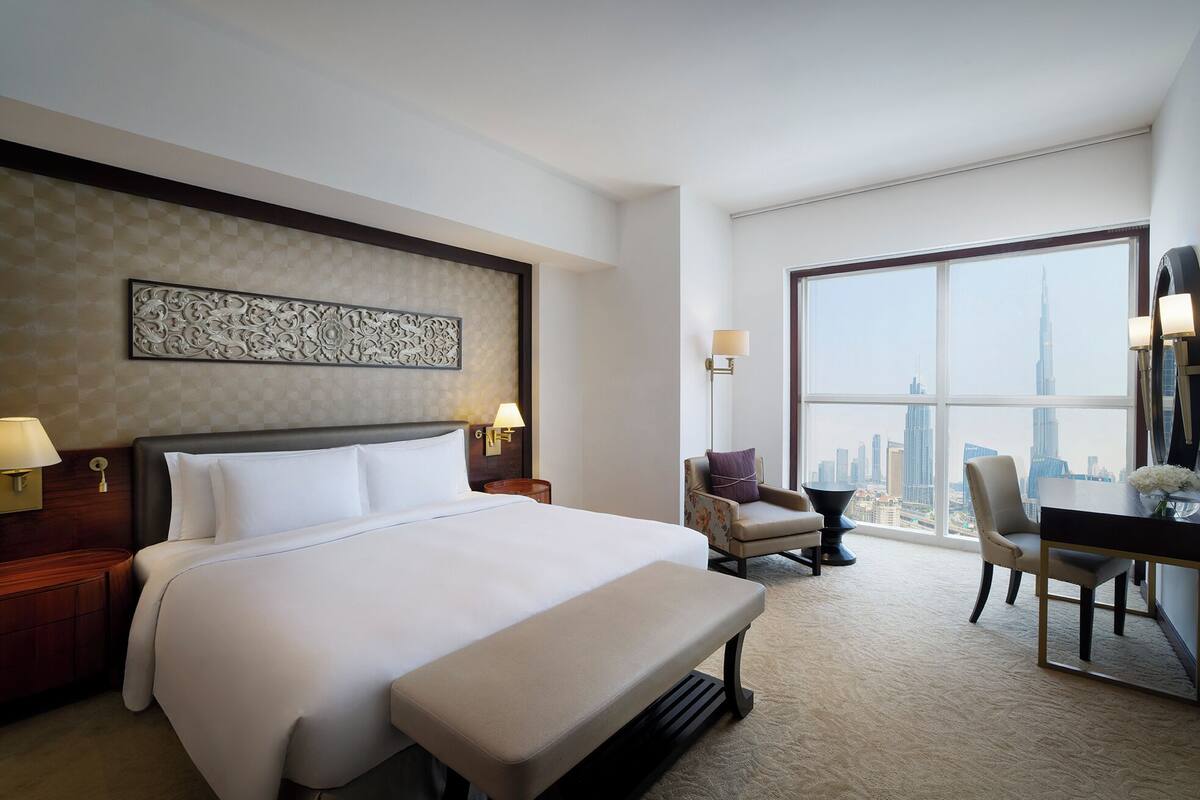 Ein Hotelzimmer mit einem großen Bett, einem Schreibtisch mit zwei Stühlen und Blick auf die Stadtlandschaft sowie einer Wanddekoration.