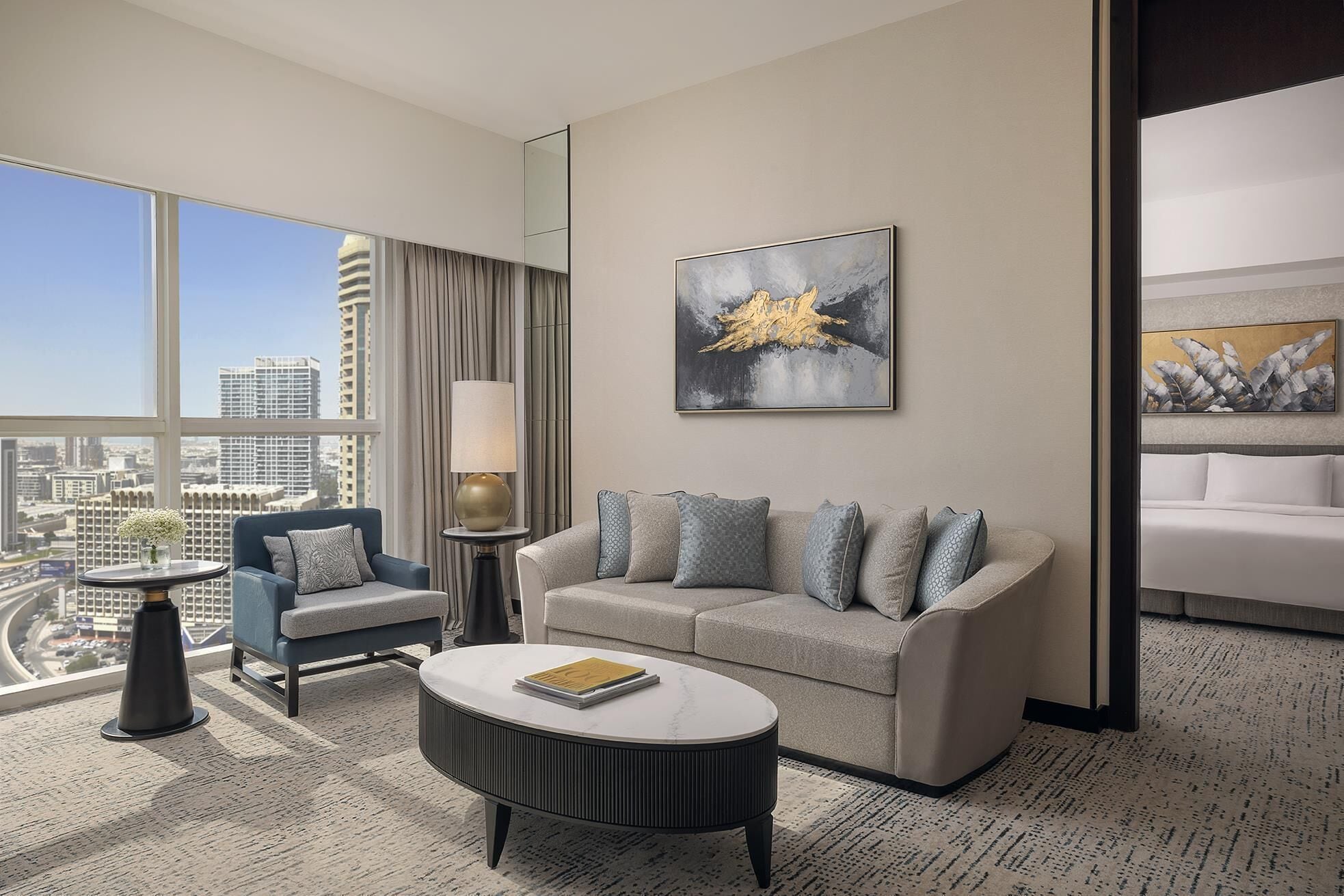 A modern hotel room with a sofa, armchair, round coffee table, and artwork on the walls.