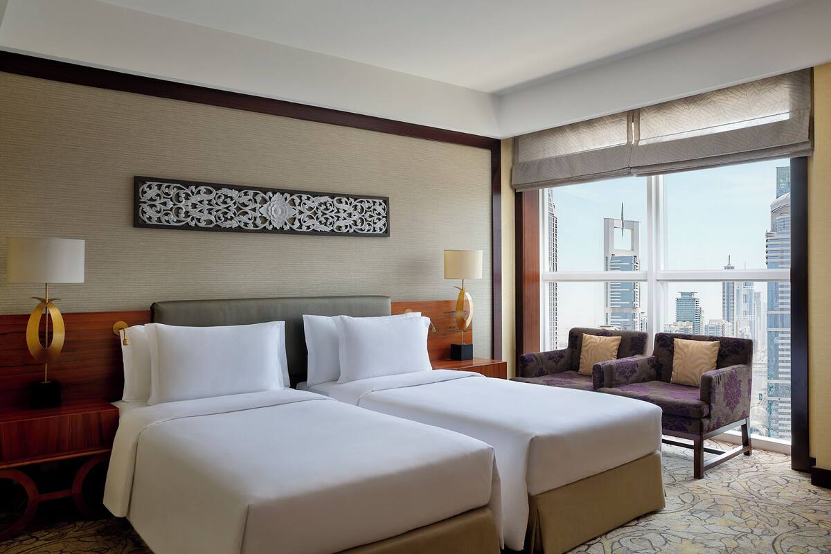 Ein Hotelzimmer mit zwei Betten, einer Schlafcouch, einem großen Fenster mit Blick auf die Stadt und einem dekorativen Wandbild.