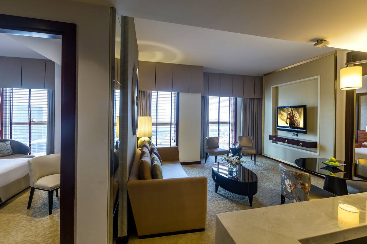Ein Hotelzimmer mit Bett, Sofa, Sessel, Fernseher und einem Essbereich mit Tisch und Stühlen.