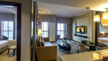Una habitación de hotel con cama, sofá, sillón, televisor y un comedor con mesa y sillas.