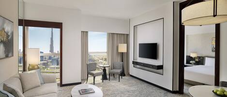 Habitación de hotel con un ventanal grande, televisor de pantalla plana, una mesa de comedor y un sofá.