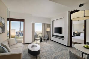 A hotel room with a large window, a flat-screen TV, a dining table, and a sofa.