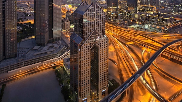 A cityscape with modern skyscrapers, including a prominent tower, and a complex highway interchange.