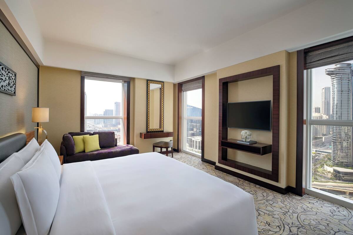 Ein Hotelzimmer mit einem großen Bett, einer Couch, einem Fernseher und Blick auf die Stadt.