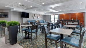 A modern restaurant with multiple tables and chairs, a flat-screen TV mounted on the wall, and a patterned floor. - Best Western Plus McAllen Airport Hotel (McAllen)