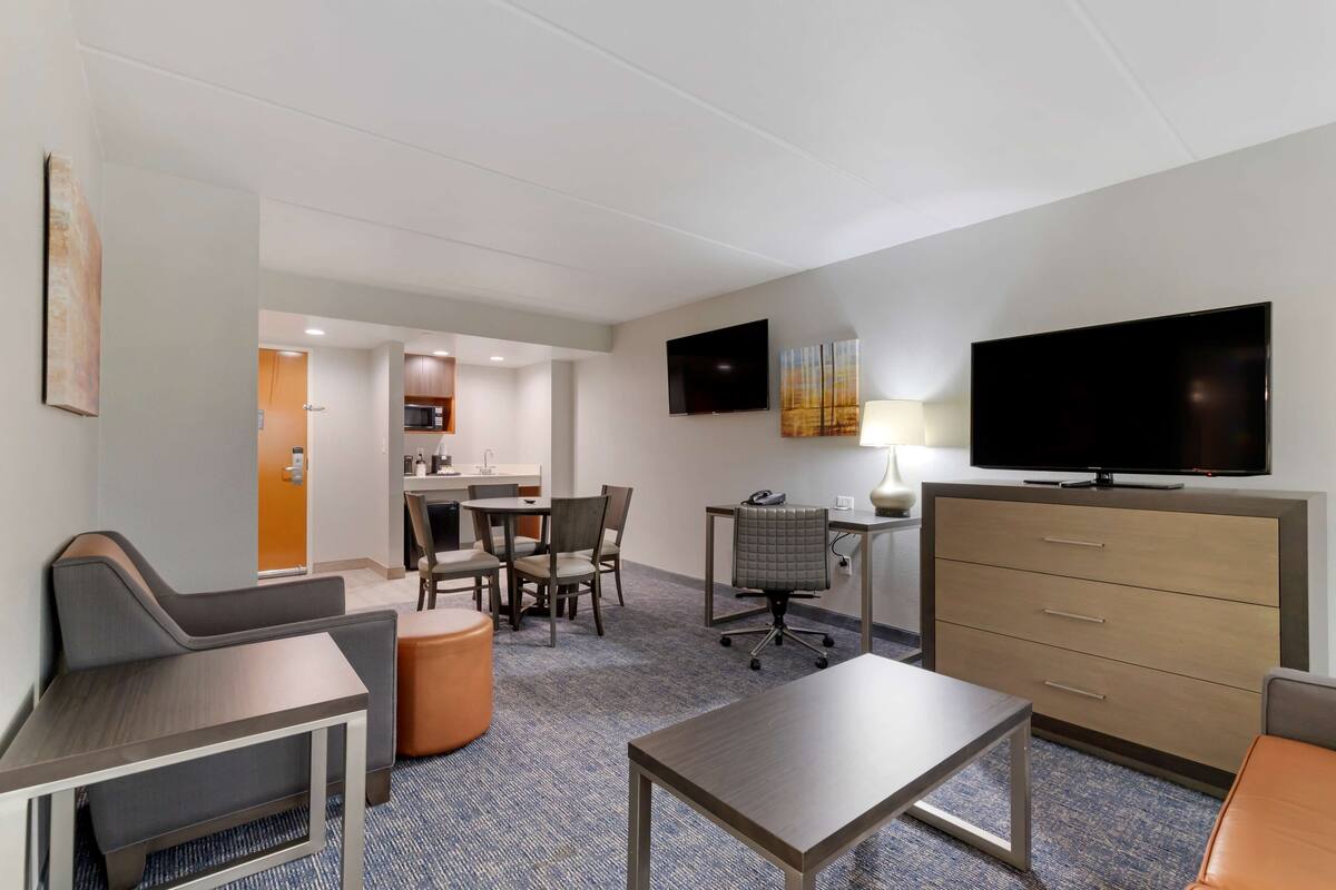 Een hotelkamer met kitchenette, een eethoek, televisie, bureau en een comfortabele zithoek.