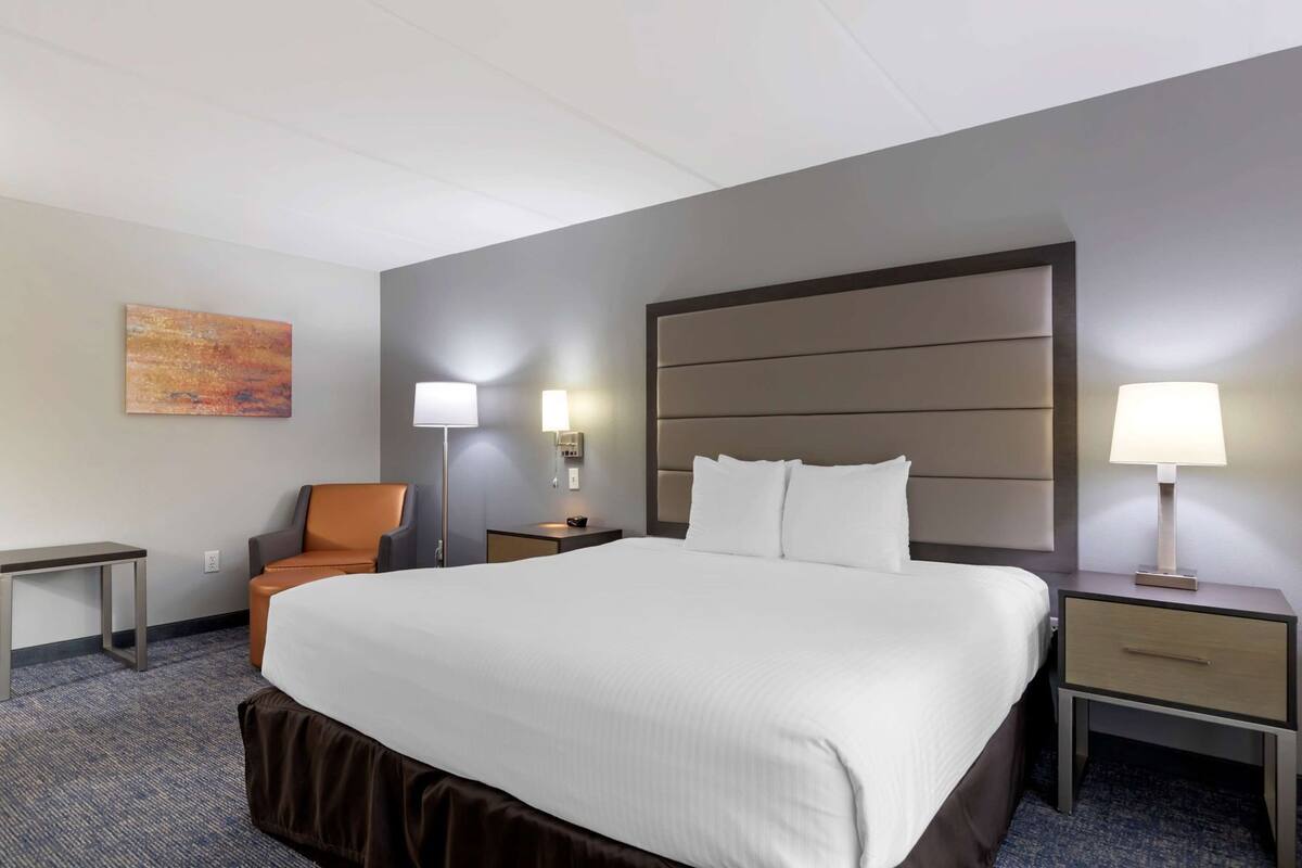 Een hotelkamer met een groot bed, twee nachtkastjes, een bureau, een stoel en een wandlamp.