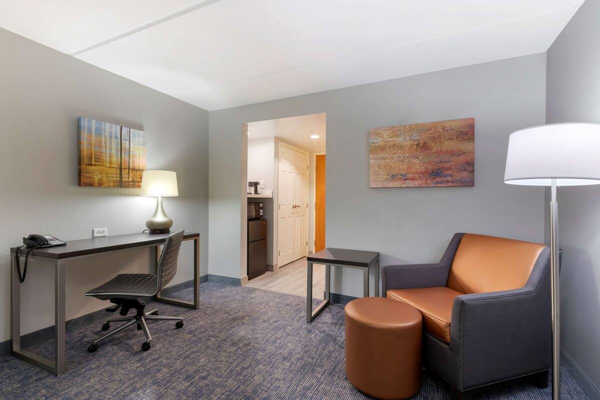 Een hotelkamer met een bureau, bureaustoel en een bank. Er is een lamp, een telefoon en kunst aan de muur.