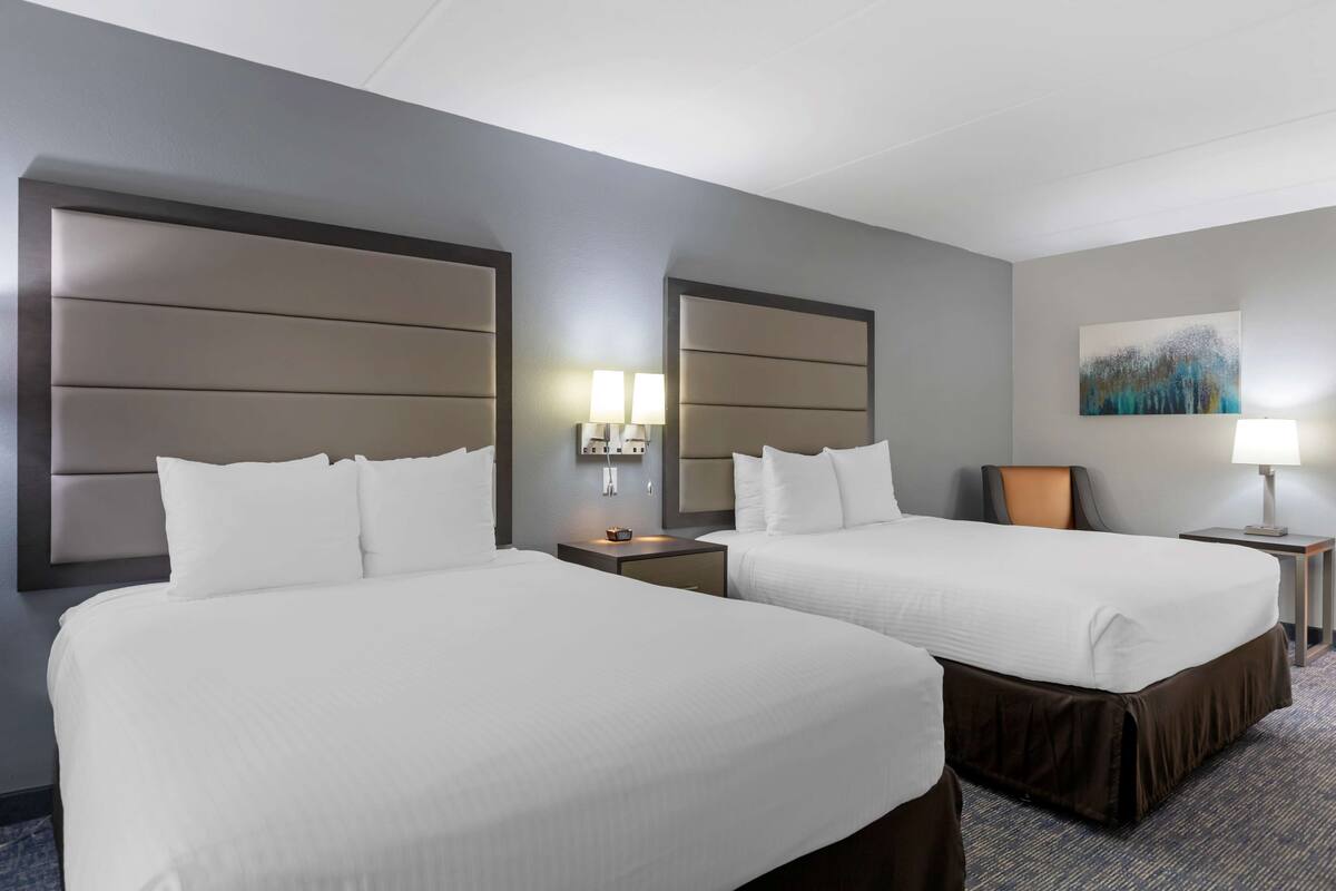 Een hotelkamer met twee bedden, een nachtkastje met een lamp en een schilderij aan de muur.