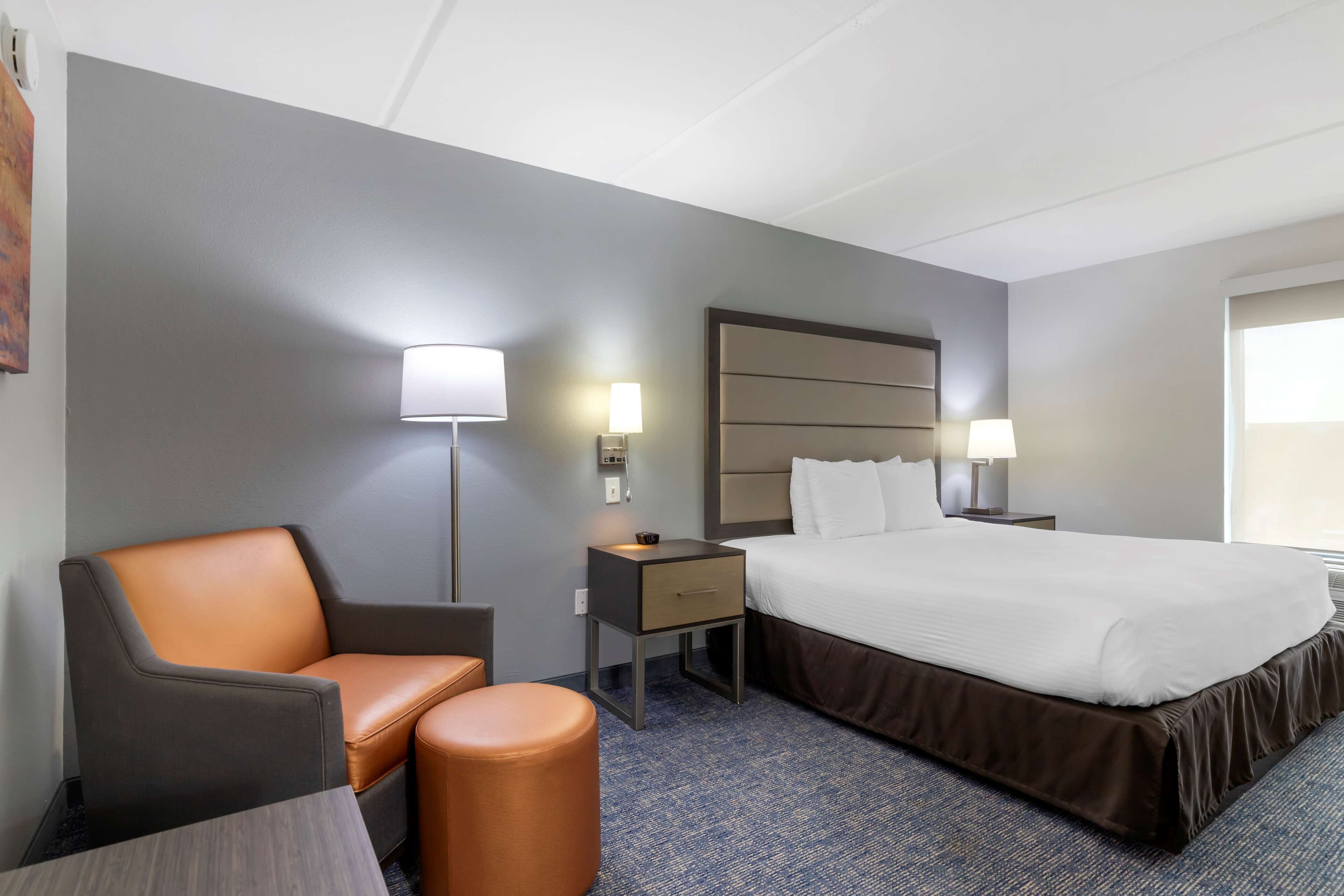 Una habitación de hotel con una cama, una silla, una mesita de noche y una lámpara.
