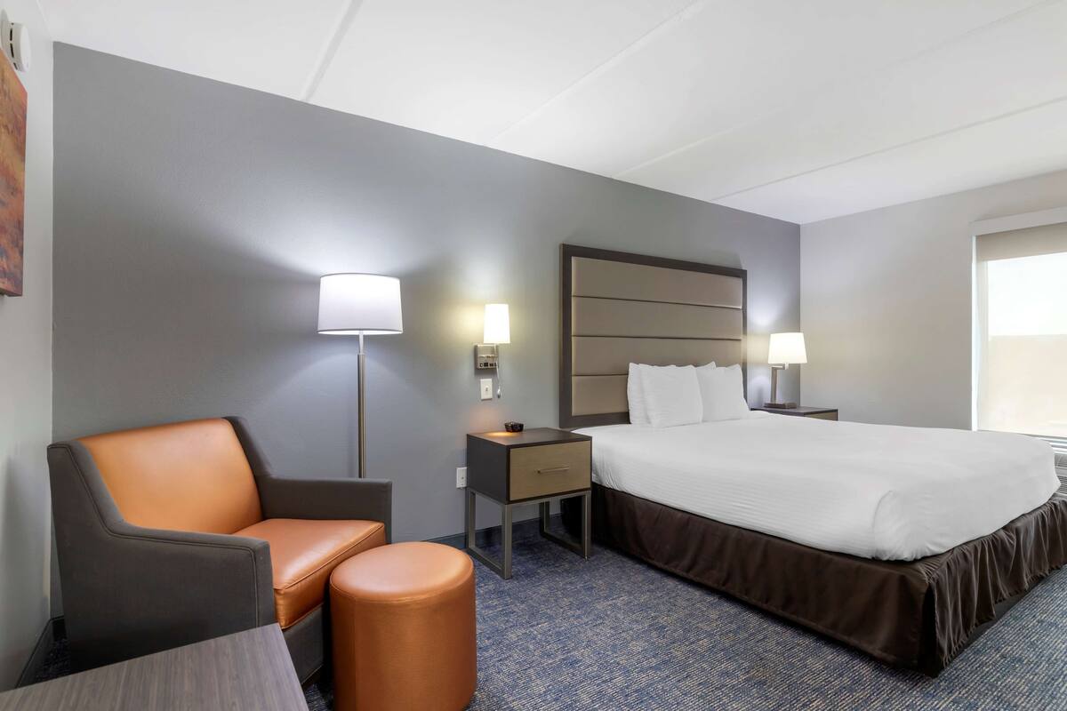 Een hotelkamer met een bed, een stoel, een nachtkastje en een lamp.