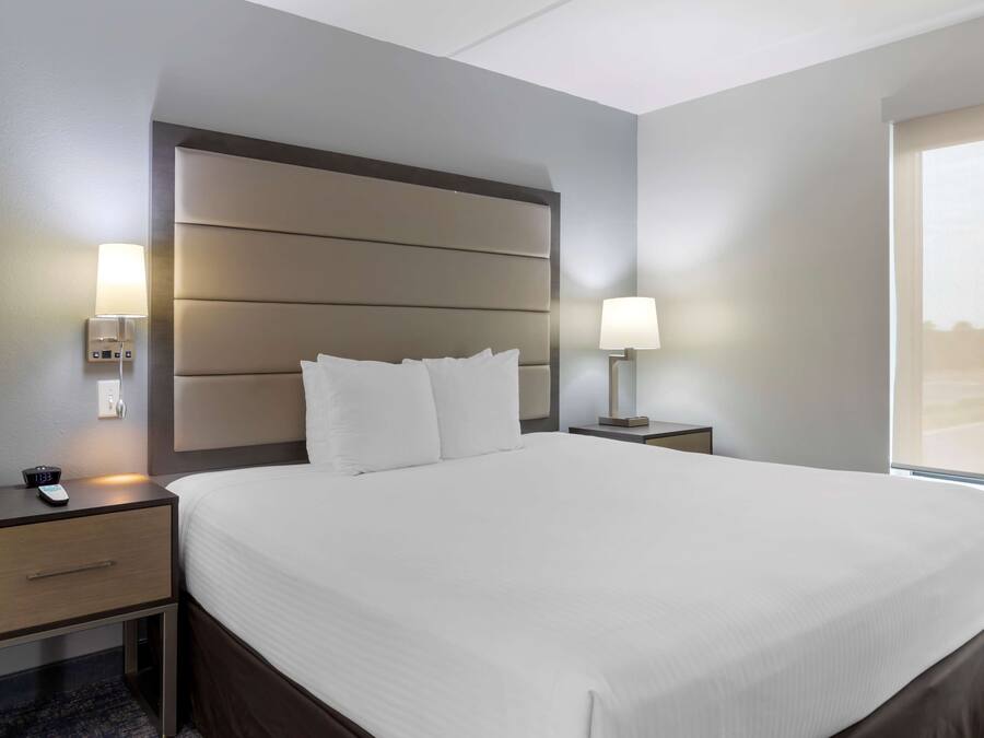 A hotel room with a large bed, bedside tables, a nightstand, a lamp, and a window with a view.