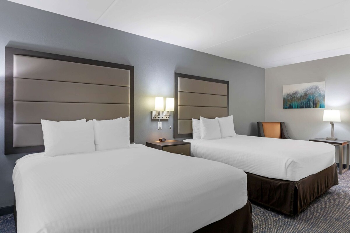 Une chambre d’hôtel avec deux lits, une tête de lit, des tables de chevet, des lampes et un tableau au mur.