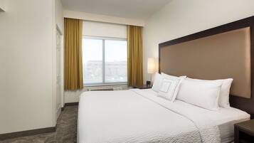 A hotel room with a large bed, a headboard, a nightstand, a lamp, and a window with curtains.