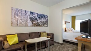 Ett hotellrum med en soffa, ett litet bord, en tv och en stor, abstrakt målning på väggen.