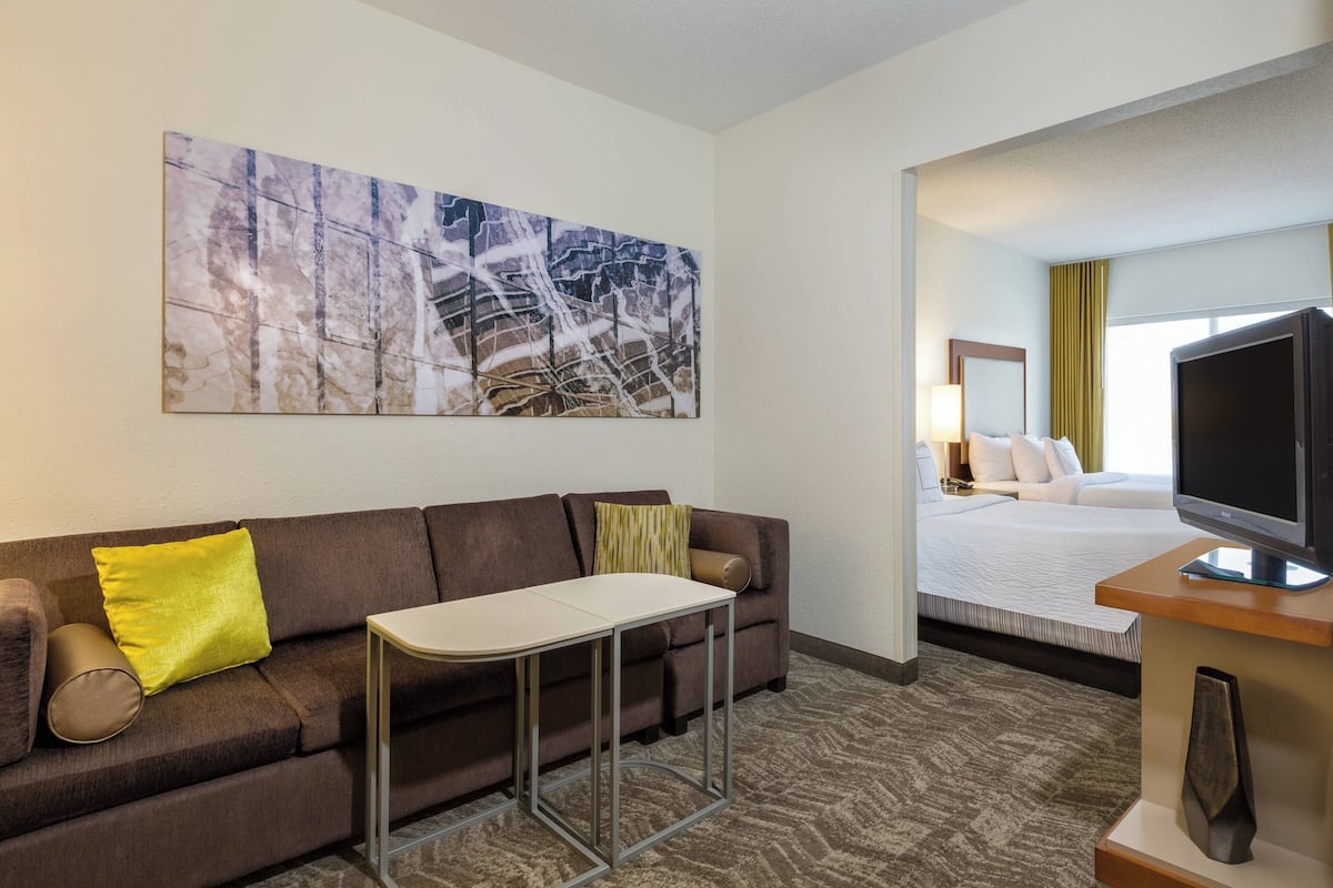 Ein Hotelzimmer mit einer Couch, einem kleinen Tisch, einem Fernseher und einem großen abstrakten Gemälde an der Wand.
