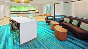 En modern hotellobby med en receptionsdisk, en sittgrupp och en stor spegelvägg.