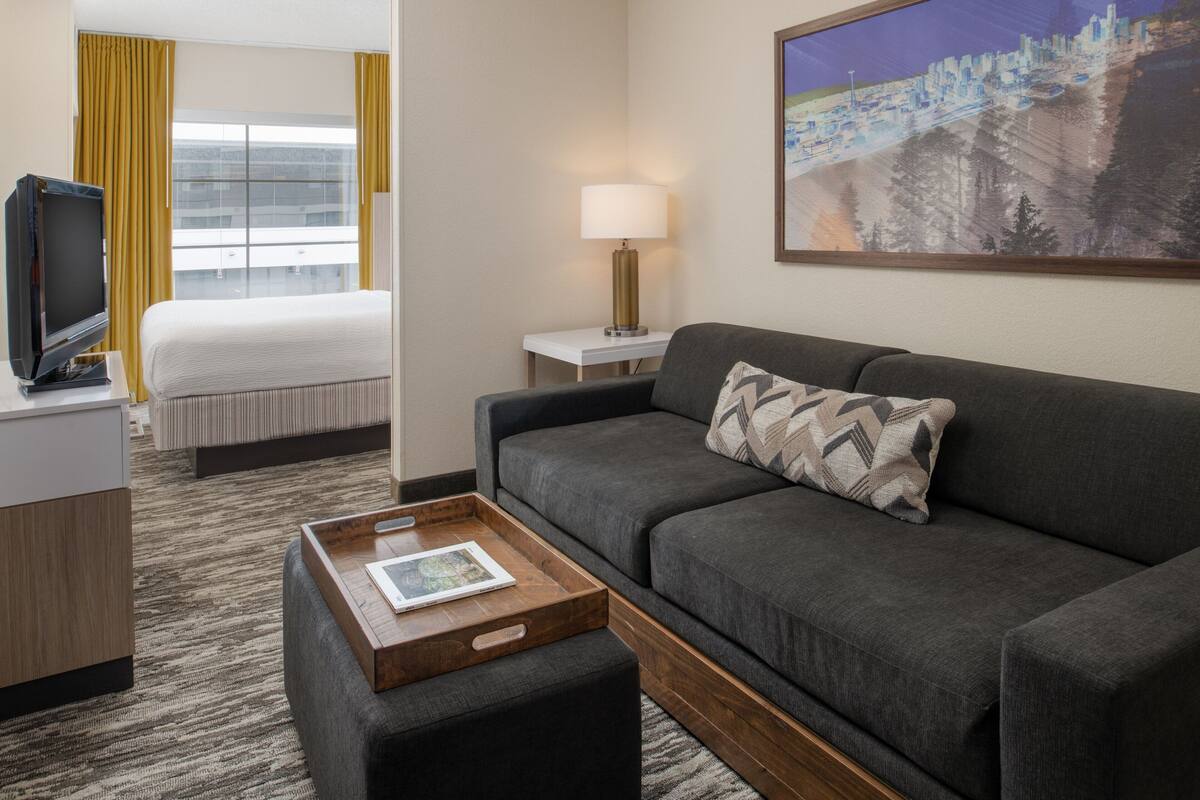 A hotel room with a bed, a sofa, a TV, a lamp, and a painting on the wall.
