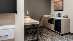 A compact hotel room with a kitchenette, a desk, a chair, a small refrigerator, and a painting on the wall. - SpringHill Suites by Marriott Seattle Downtown/South Lake Union (Seattle)