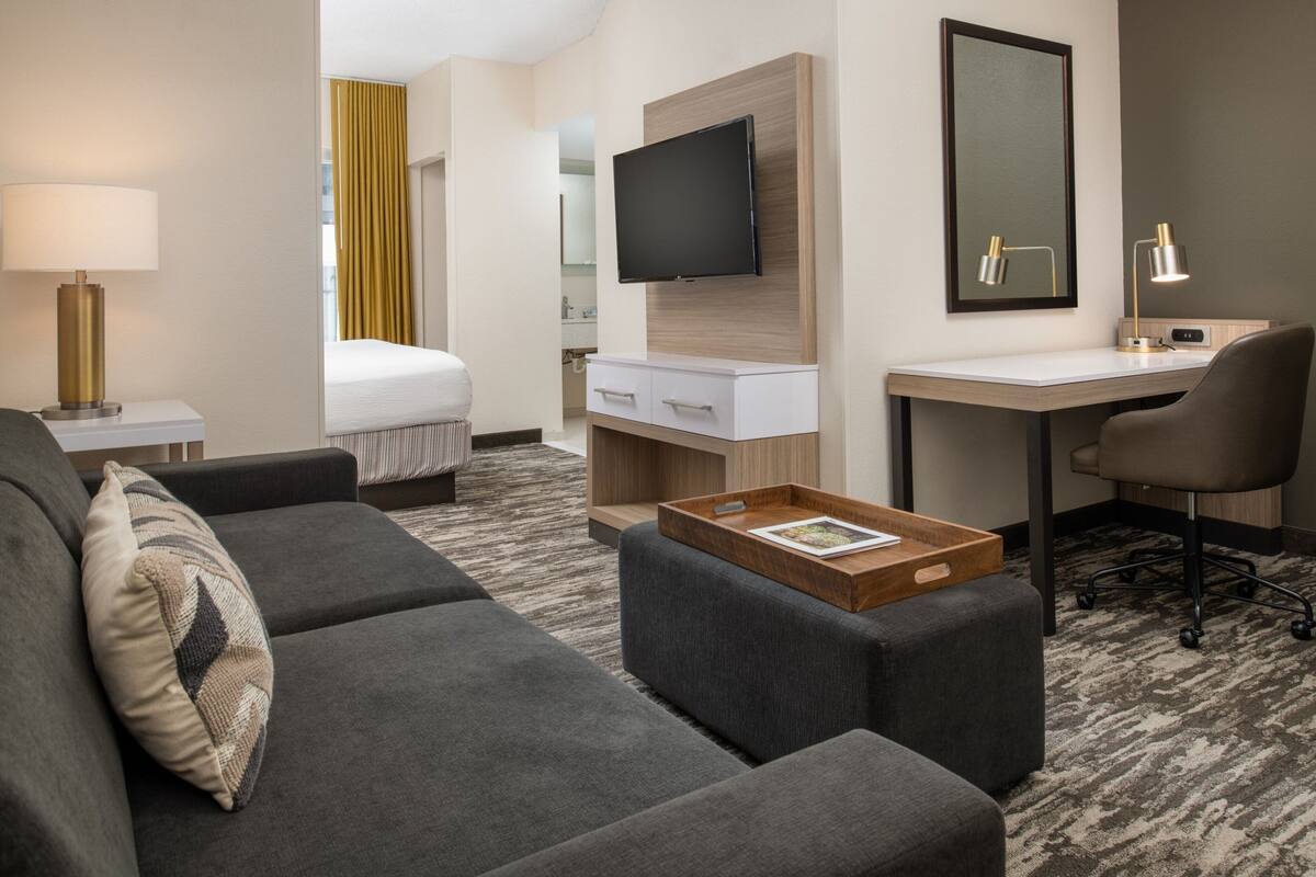 A hotel room with a sofa, a desk, a TV, a mirror, and a bed.